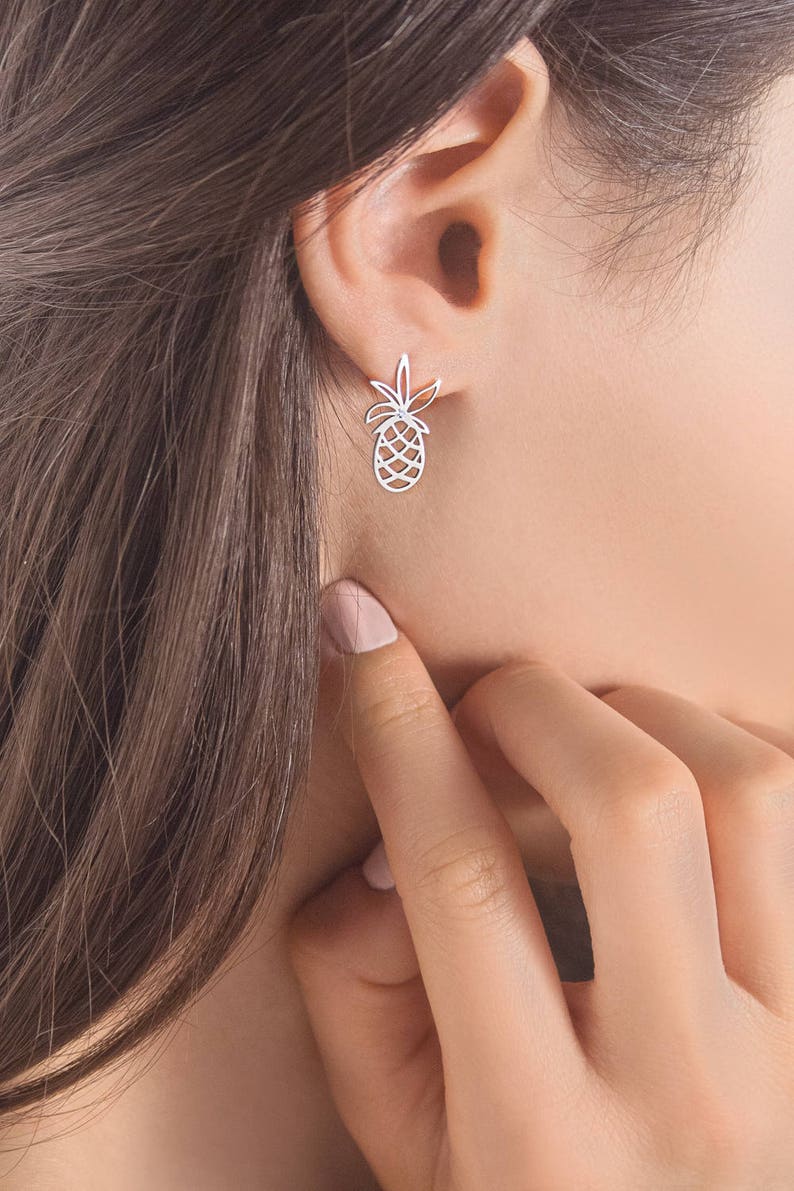 A delicate white gold pineapple stud earring with a white natural diamond in the center of the leaves is shown worn by a model.