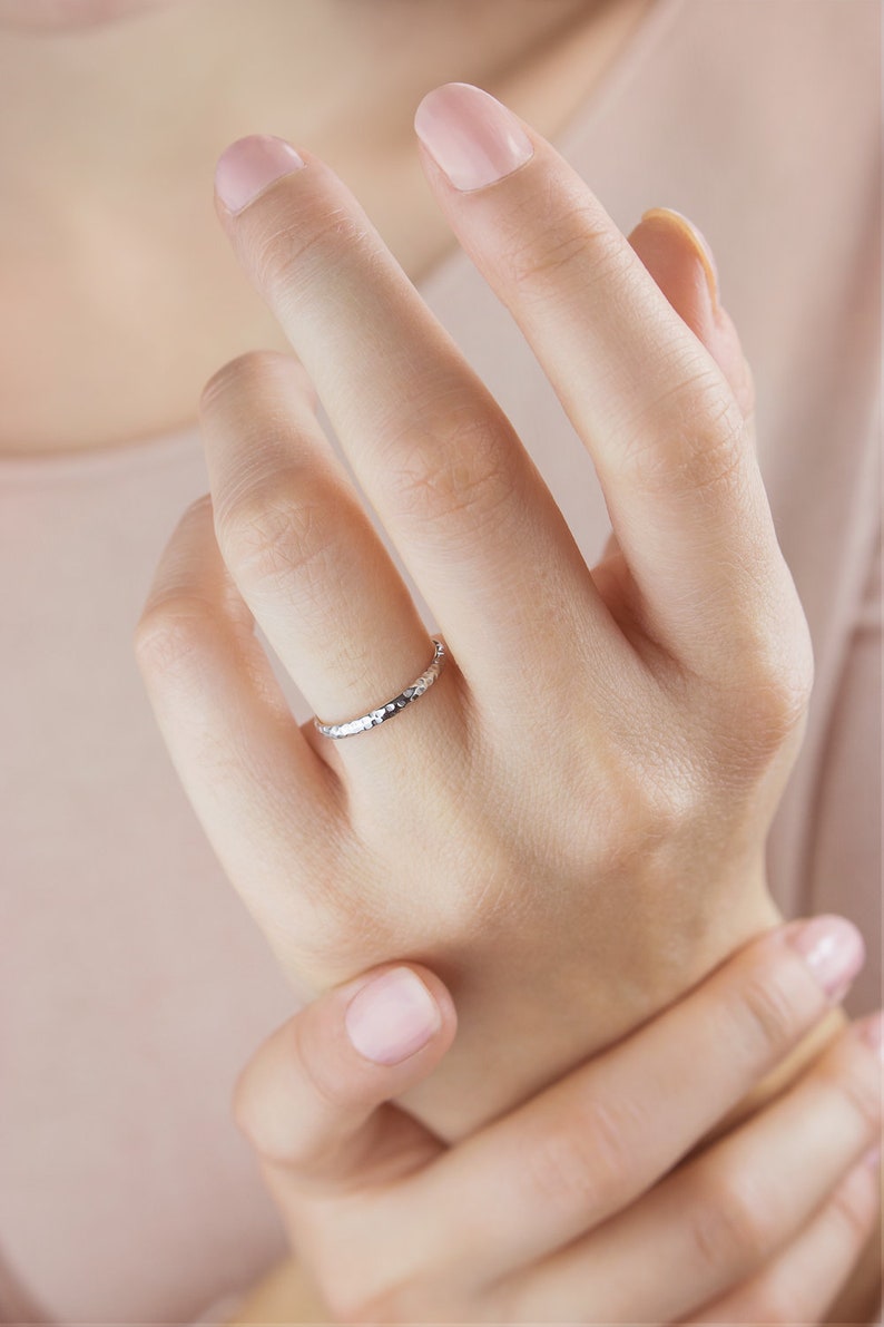 A yellow gold ring with a hammered surface on the outer part and a pished on the inside is laid beautifully shown worn by a model.