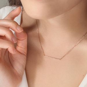 A minimalist style yellow gold necklace with a thin cable chain and a thin bar with natural white diamonds embedded on it worn by a model.