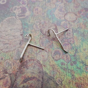 Puede incluir: Un par de pendientes de plata en forma de diseño abstracto simple. Los pendientes están hechos de metal fino y tienen una forma ligeramente curvada.