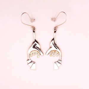 May include: A pair of silver dangle earrings with a gold accent. The earrings are shaped like a stylized bird with a gold drip design.
