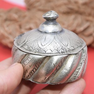 May include: A silver trinket box with an ornate, engraved lid and a twisted, textured base. The box is small and has a domed lid.