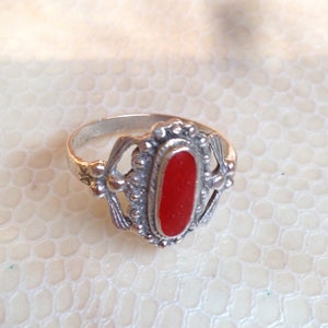 Peut inclure: Une bague en argent avec une pierre rouge ovale sertie dans un motif de filigrane d&eacute;coratif.