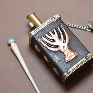 May include: A small wooden box with a metal menorah design on the front. The box has a gold trim and a chain attached to a small metal ring. A white stick with a turquoise tip is also in the image.