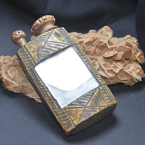May include: A wooden bottle with a carved design and a mirrored surface. The bottle has two wooden stoppers and is resting on a brown rock.