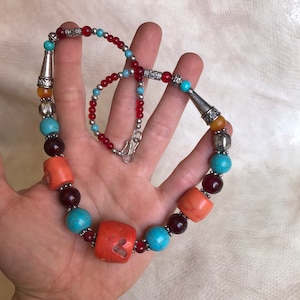 K&ouml;nnte beinhalten: Eine mehrfarbige Perlenkette mit t&uuml;rkisfarbenen, roten, orangefarbenen und bernsteinfarbenen Perlen. Die Kette hat silberne Akzente und einen Verschluss.