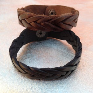May include: Two braided leather bracelets, one black and one brown. Both bracelets have a snap closure.