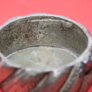 May include: A silver metal container with a twisted design and a lid. The inside of the container is empty and shows signs of wear.