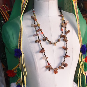 May include: A white mannequin wearing a green shawl with colourful tassels and a long necklace made of brown, red and orange stones.