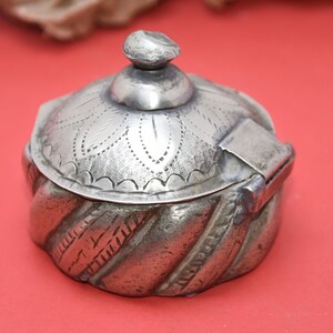 May include: A silver trinket box with a hinged lid and intricate engraved designs. The box has a rounded shape and a domed lid with a floral pattern.
