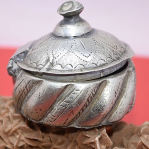 May include: A silver, intricately engraved, hinged box with a domed lid. The box has a swirling, textured pattern on the bottom half and a floral design on the lid.