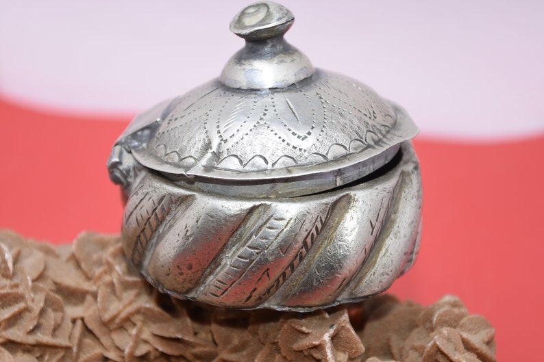 May include: A silver, intricately engraved, hinged box with a domed lid. The box has a swirling, textured pattern on the bottom half and a floral design on the lid.