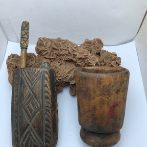 Puede incluir: Un conjunto de dos herramientas de madera, una con un mango tallado y un cuerpo rectangular, la otra un mortero en forma de taza. Ambas herramientas son de color marrón y tienen un aspecto rústico.