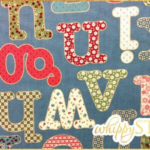 May include: A blue fabric with a patchwork alphabet design. The letters are in various colors and patterns, including red, green, and white. The letters are outlined in a darker color. The fabric has a subtle texture. The text "whippySTIX" is in gold lettering in the bottom right corner.