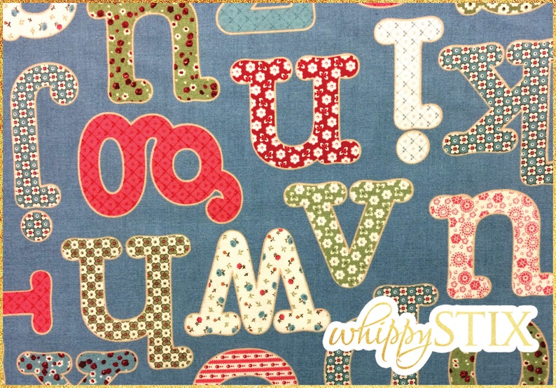 May include: A blue fabric with a patchwork alphabet design. The letters are in various colors and patterns, including red, green, and white. The letters are outlined in a darker color. The fabric has a subtle texture. The text "whippySTIX" is in gold lettering in the bottom right corner.