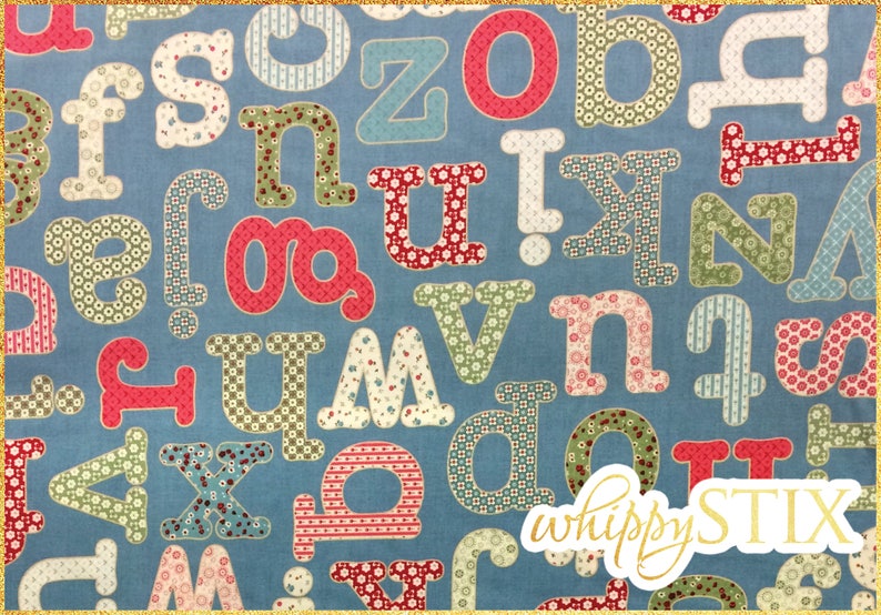 May include: A blue fabric with a pattern of colorful letters in different fonts and sizes. The letters are made of patchwork fabric with various patterns. The fabric is labeled "whippy STIX".