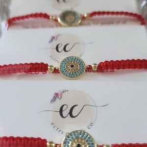May include: Red string bracelet with a gold evil eye charm. The bracelet is made for people of all faiths as a powerful shield of protection against unwanted energy.  The text on the card reads: "Red String Bracelet is made for people of all faiths as a powerful shield of protection against unwanted energy. Regardless of your spiritual background, you can wear our Red String to boost your personal power. Tie it on your left wrist."