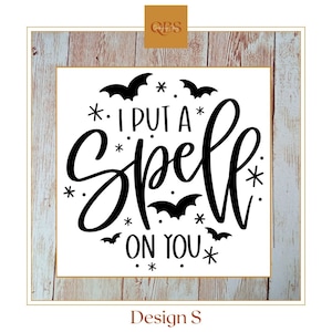 Puede incluir: Un letrero cuadrado blanco con la frase "I PUT A SPELL ON YOU" en escritura negra, rodeado de murciélagos y estrellas. El letrero está enmarcado con un borde de madera clara y un borde interior dorado. El texto "Design S" está en la parte inferior.