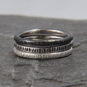 May include: Three silver rings stacked on top of each other. The top ring is black, the middle ring is silver, and the bottom ring is silver.