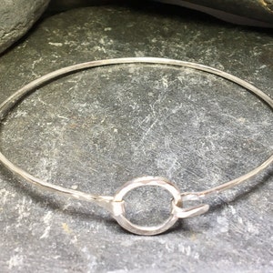 Könnte beinhalten: Ein silbernes Armreif-Armband mit gehämmerter Oberfläche und einem runden Verschluss.