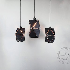 May include: Three black geometric pendant lights with brass accents hang from black cords against a white wall. The lights are arranged in a triangular formation. The logo "21neun Interior Design & Architecture" with the fraction "21/9" is visible in the bottom right corner of the image.