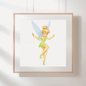 May include: A framed cross-stitch of Tinkerbell, a fairy with blonde hair, green dress, and blue wings. The artwork is displayed in a light-colored wooden frame, hanging on a white wall. The fairy is in a dancing pose.