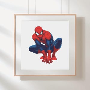 May include: A framed print featuring a pixelated illustration of Spider-Man in a crouching pose. The superhero is depicted in his classic red and blue suit, with white eyes and a webbed design. The artwork is set against a white background.