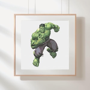 Op de afbeelding: Een ingelijst kruissteekkunstwerk met de Hulk in een dynamische pose. De Hulk is afgebeeld in groentinten met grijze en paarse kleding. Het kunstwerk wordt gepresenteerd in een lichtbruine houten lijst.