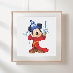 Puede incluir: Arte de punto de cruz de Mickey Mouse vestido de mago, con un sombrero azul con estrellas y una túnica roja. Sostiene una varita con chispas azules. La obra está enmarcada en un marco de madera clara.