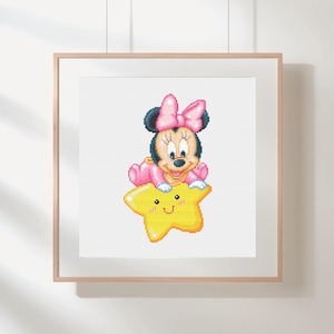 Può includere: Un ricamo a punto croce incorniciato con Minnie Mouse in abito e fiocco rosa, seduta su una stella gialla con un volto sorridente. L'opera è presentata in una cornice di legno chiaro.