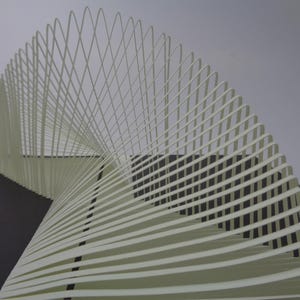 May include: Abstract sculpture composed of layered, off-white paper strips. The strips curve and intersect, creating a dynamic, three-dimensional form. The sculpture is set against a neutral background, highlighting its intricate design.