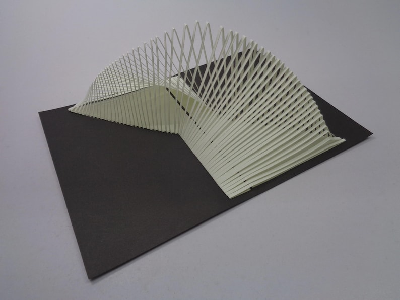 May include: A white architectural model with a curved, fan-like design. The model is constructed from thin, vertical slats and sits on a black rectangular base. The design has a modern, minimalist aesthetic.