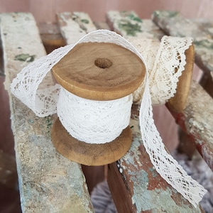 May include: Two spools of white lace ribbon wound around wooden spools. The spools are sitting on a weathered wooden surface.