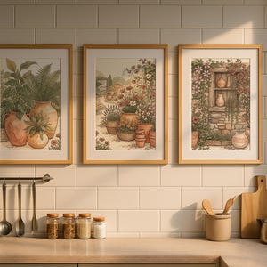 May include: Three framed wall art prints featuring botanical and garden scenes with terracotta pots, displayed in a kitchen. The prints are arranged horizontally on a white tiled wall above a counter with various kitchen utensils and jars.