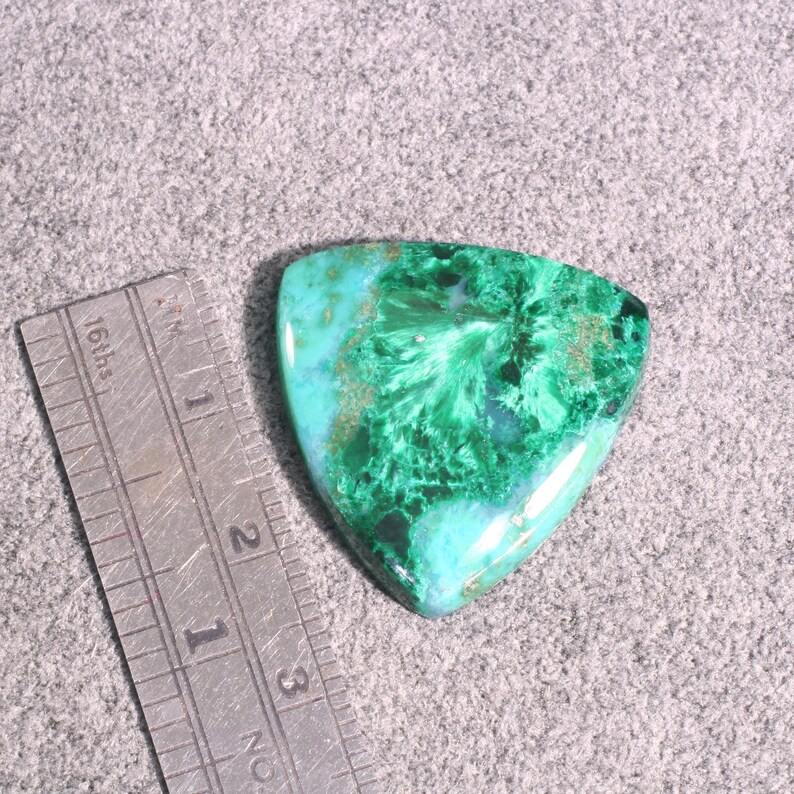 Puede incluir: Un cabuj&oacute;n de malaquita verde y azul con forma triangular. La piedra tiene un patr&oacute;n de remolino y un acabado brillante.