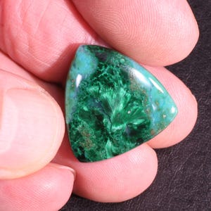Puede incluir: Una piedra preciosa cabuj&oacute;n triangular verde y marr&oacute;n con un patr&oacute;n de remolino. La piedra preciosa est&aacute; cortada en forma triangular y tiene una superficie lisa y pulida.