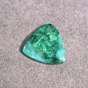 Puede incluir: Un cabuj&oacute;n triangular de piedra preciosa verde y azul con un patr&oacute;n de remolino. La piedra tiene una superficie lisa y pulida.