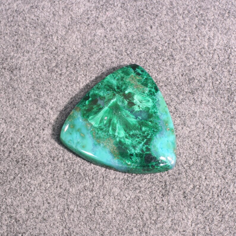 Puede incluir: Un cabuj&oacute;n triangular de piedra preciosa verde y azul con un patr&oacute;n de remolino. La piedra tiene una superficie lisa y pulida.