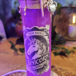 Può includere: Una bottiglia cilindrica di liquido viola con un'etichetta raffigurante un unicorno e il testo Fresh Brewed Unicorn Blood Pure Extract. La parte superiore è sigillata con gocce di cera rosa chiaro, avvolta da spago e decorata con un cuore d'argento.