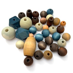 May include: A collection of wooden beads in various shapes and colors. The beads include spheres, cylinders, and faceted shapes in shades of blue, brown, beige, and orange. Each bead has a hole for stringing.