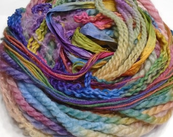 May include: A colorful skein of yarn with a variety of textures and colors. The yarn includes shades of pink, blue, green, yellow, and purple. Some strands have a metallic sheen, and ribbons are woven throughout. This yarn is suitable for various craft projects.