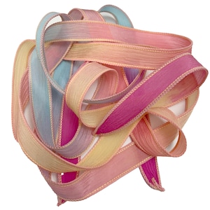 May include: A tangled bundle of colorful ribbons in shades of pink, yellow, peach, and blue. The ribbons have a textured appearance and are edged with a delicate, light-colored trim. The overall effect is soft and pastel-like.