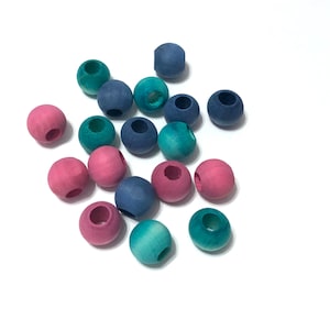 May include: A collection of colorful wooden beads in shades of pink, teal, and blue. Each bead is round with a large hole through the center. The beads are scattered on a white surface.