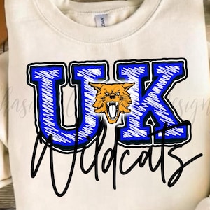 May include: Cream-colored sweatshirt with a blue and black "UK Wildcats" graphic. The letters "UK" are in blue with a black outline, and a snarling orange wildcat is in the center. The word "Wildcats" is in black script.
