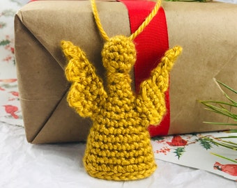 Könnte beinhalten: Ein gehäkelter goldener Engel-Anhänger mit Flügeln, der an einer braunen Geschenkbox mit rotem Band hängt.