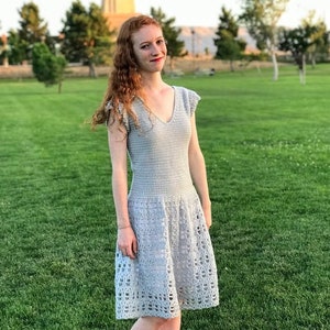 Puede incluir: Una mujer con un vestido de crochet gris claro con cuello en V y falda acampanada.
