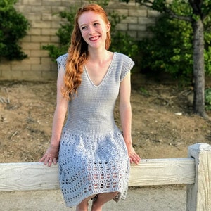 Puede incluir: Una mujer lleva un vestido de crochet gris claro con cuello en V y mangas cortas. El vestido tiene un patr&oacute;n de encaje de crochet en la falda.
