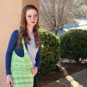 Puede incluir: Una mujer con un su&eacute;ter azul y una bolsa de mano de crochet verde. La bolsa tiene un dise&ntilde;o &uacute;nico con una variedad de puntadas.