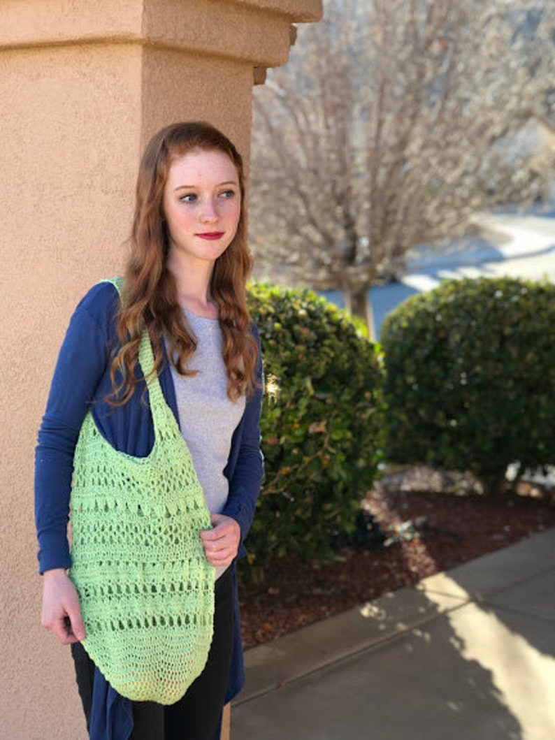 Puede incluir: Una mujer con un su&eacute;ter azul y una bolsa de mano de crochet verde. La bolsa tiene un dise&ntilde;o &uacute;nico con una variedad de puntadas.