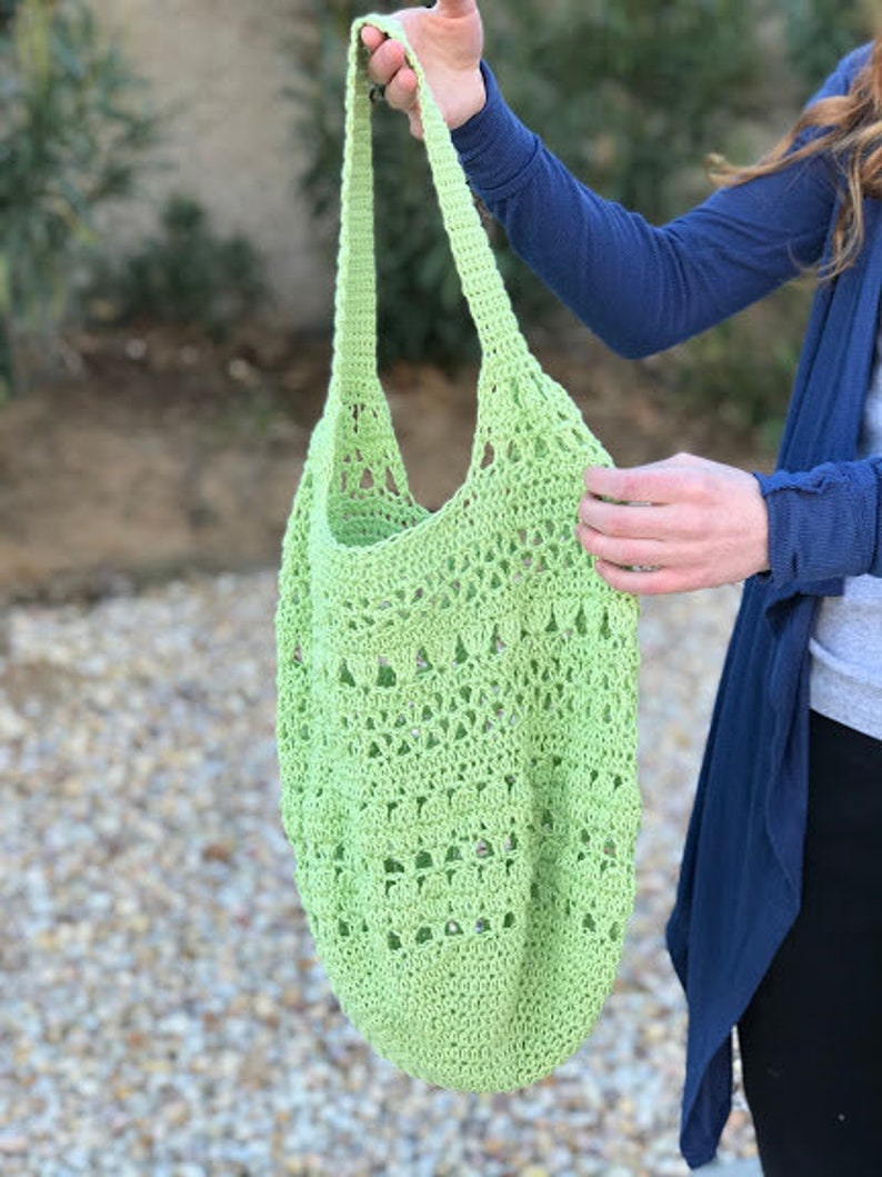 Puede incluir: Una bolsa de mano de crochet de color verde claro con un patr&oacute;n delicado. La bolsa tiene una sola correa y es lo suficientemente grande como para llevar comestibles u otros art&iacute;culos.